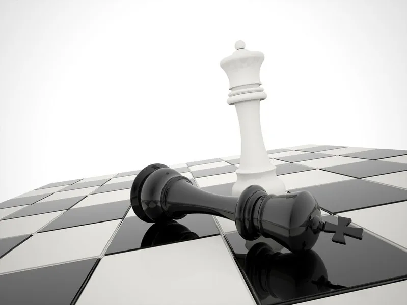 White chess queen standing over a toppled black king on a chessboard