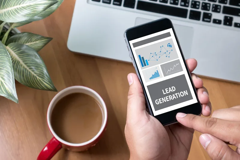 Lead generation analytics dashboard on a smartphone beside a laptop and coffee