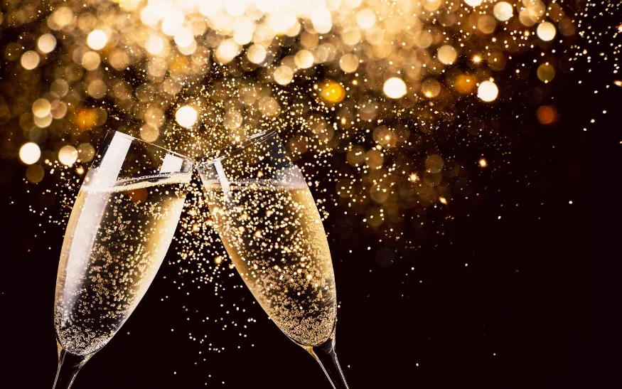 Two champagne flutes toasting against golden celebratory bokeh lights